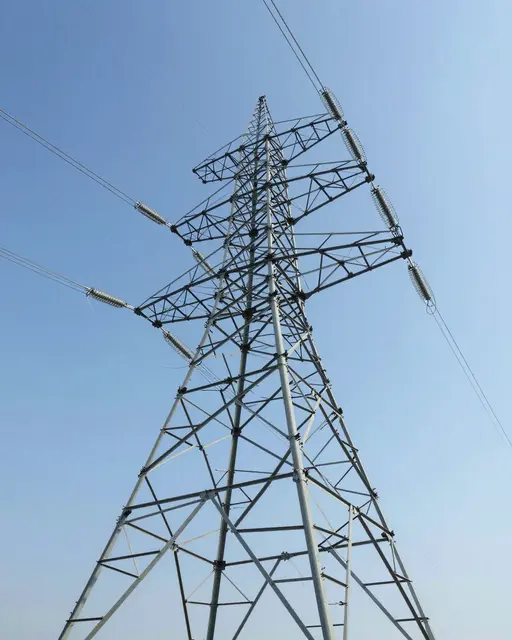 Low angle upward view of a steel high-voltage electricity pylon against a clear pale blue sky