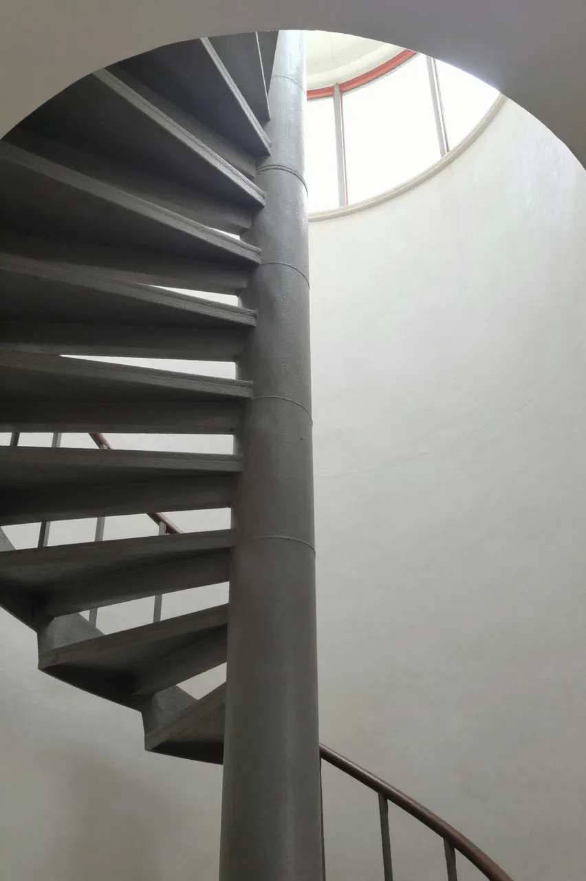 Low angle view of a concrete spiral staircase leading up to a circular ceiling skylight