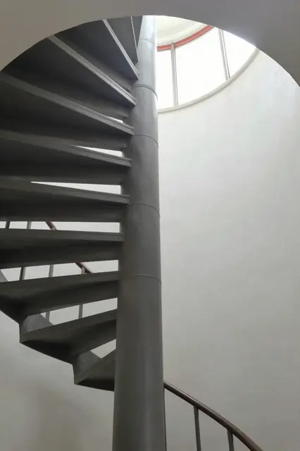 Low angle view of a concrete spiral staircase leading up to a circular ceiling skylight