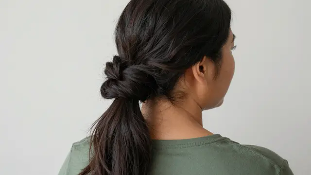 Rear three-quarter view of a woman with a twisted hair updo wearing a moss green top against a plain wall