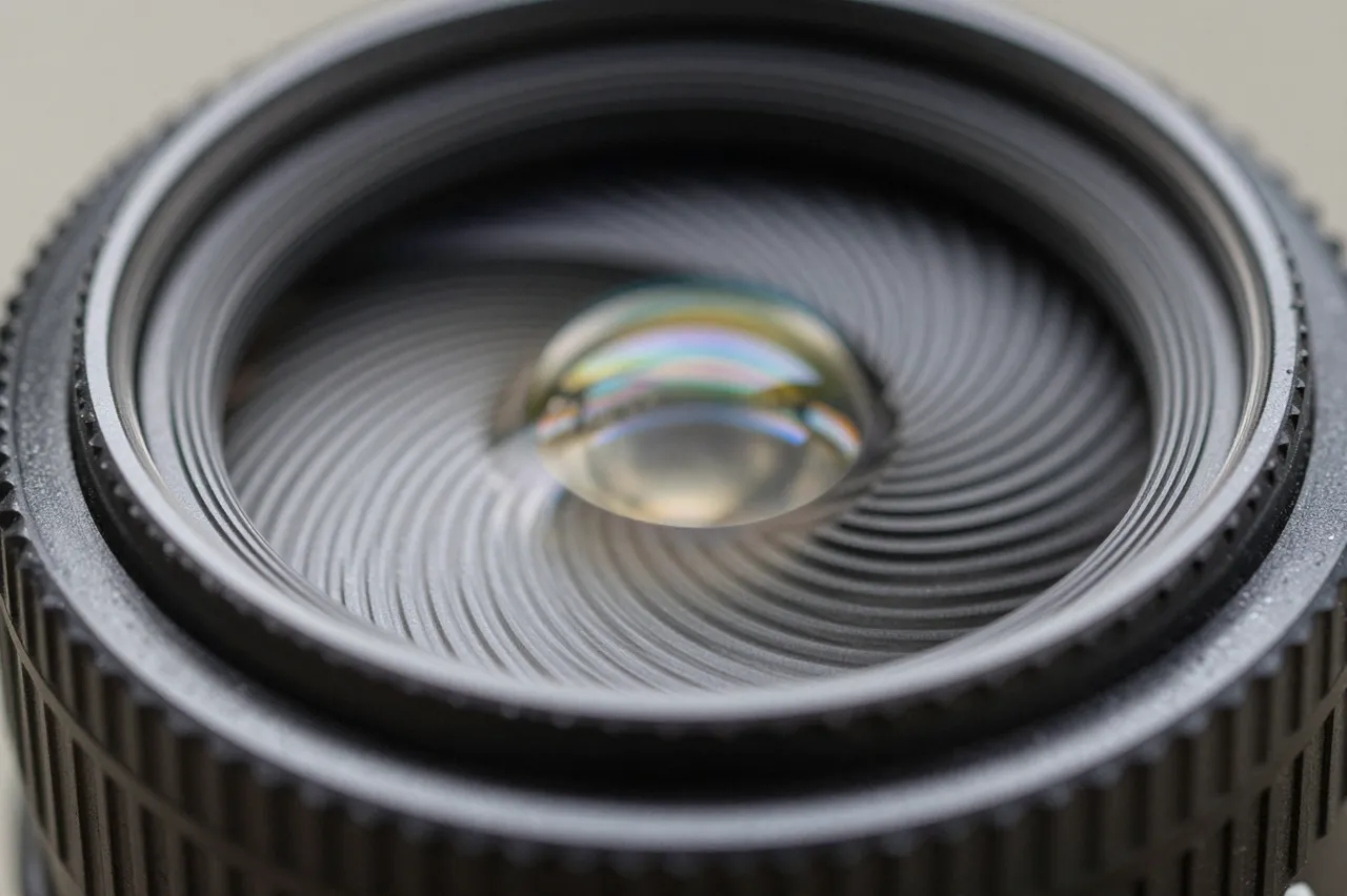 Close up macro shot of the front glass element of a camera lens with iridescent light refraction