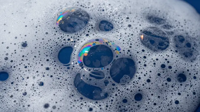 Close-up macro view of iridescent soap bubbles resting in white foam against dark blue