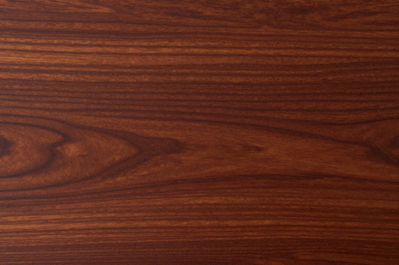 Full frame close-up of rich deep red-brown mahogany wood grain with natural flowing patterns.