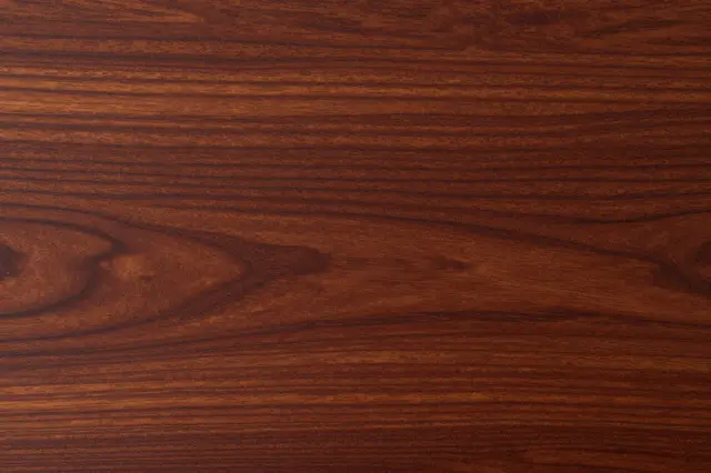 Full frame close-up of rich deep red-brown mahogany wood grain with natural flowing patterns.