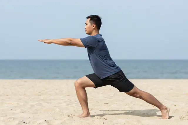 Side view of a Southeast Asian man stretching while standing on a sunny sandy beach