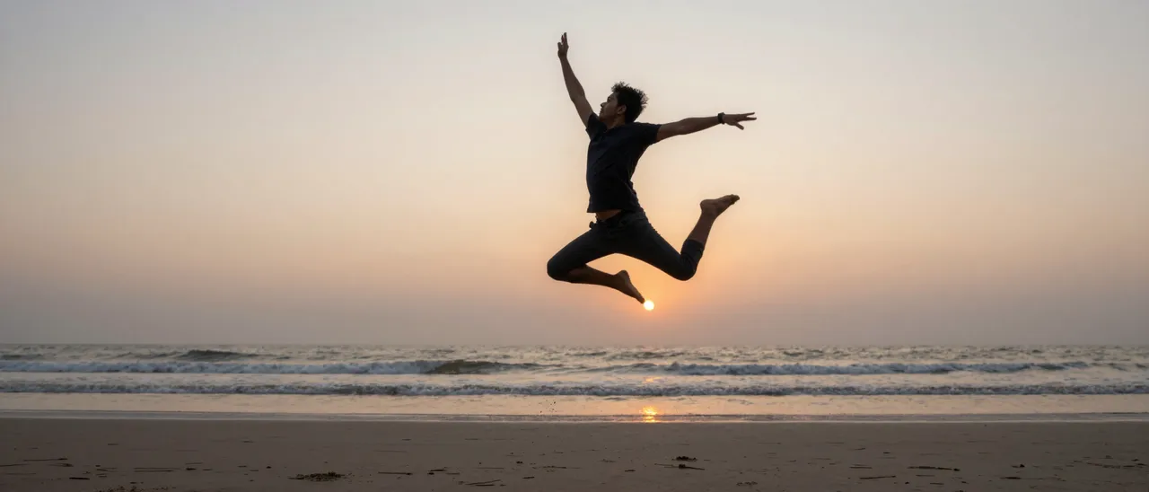 Silhouette of a man mid-leap in the air above a quiet beach as the sun sets over the ocean