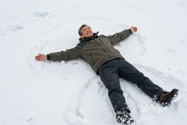 Overhead view of a smiling older man lying on fresh snow making a snow angel