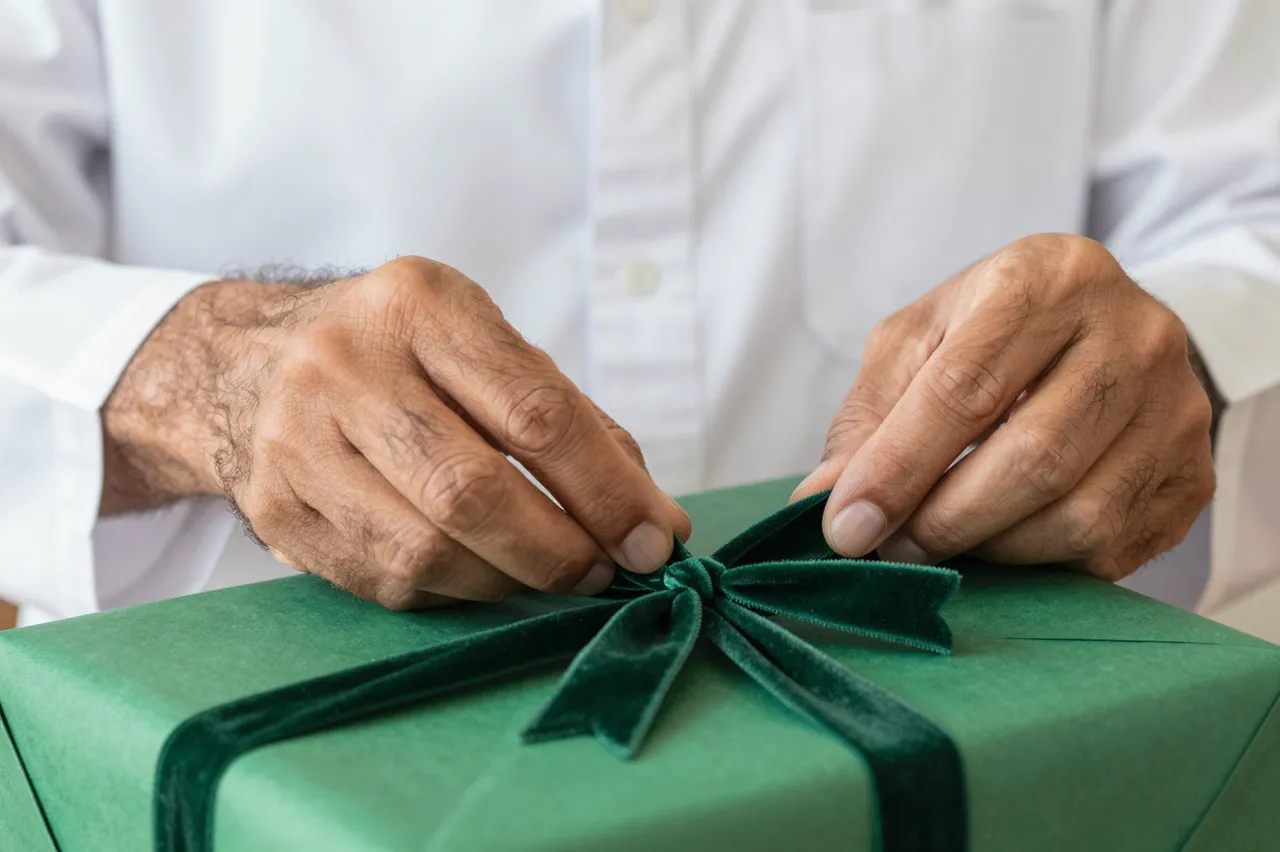 Hands of an older man adjusting a dark green velvet ribbon bow on a green wrapped gift box
