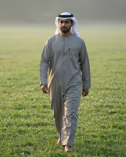 A Middle Eastern man walks barefoot across dewy grass in soft early morning light