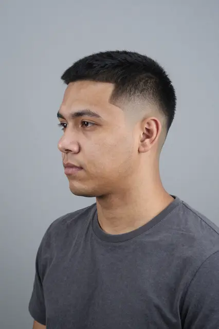 Three-quarter profile portrait of a late twenties Latino man with a low fade haircut against a plain grey backdrop