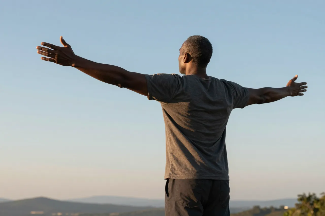 Rear view of a middle aged Black man standing on a hilltop with arms spread wide as the sun rises