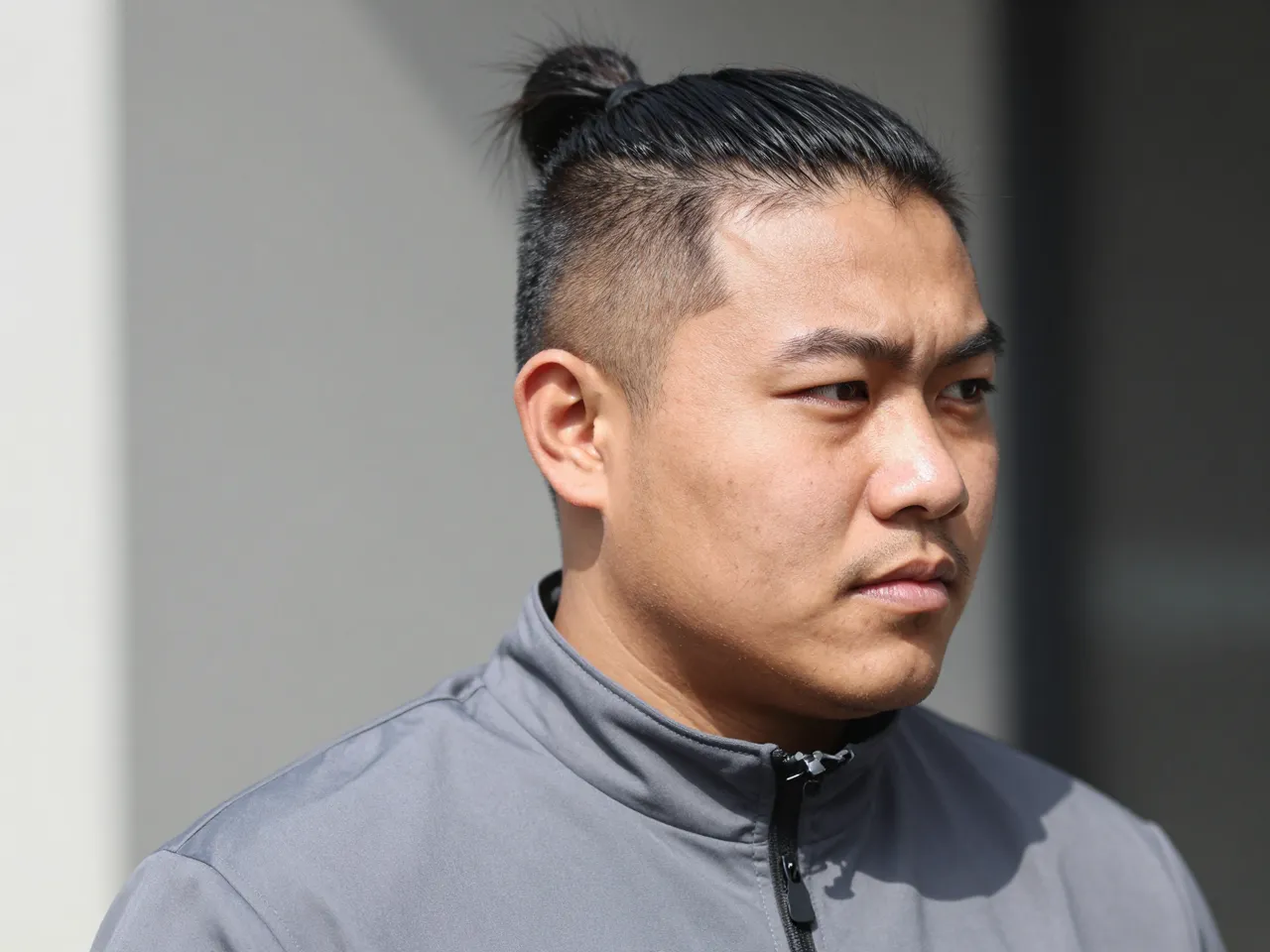 Outdoor close-up portrait of an Indigenous man in his thirties wearing a grey zip-up jacket in bright daylight