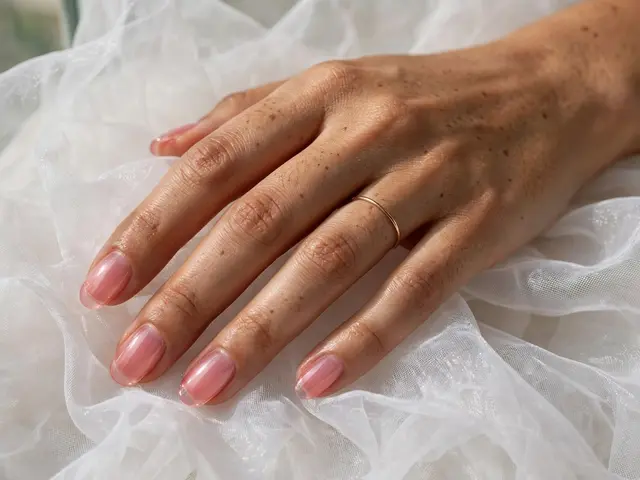 A woman's hand with translucent pink oval jelly nails rests gently on sheer white organza fabric.