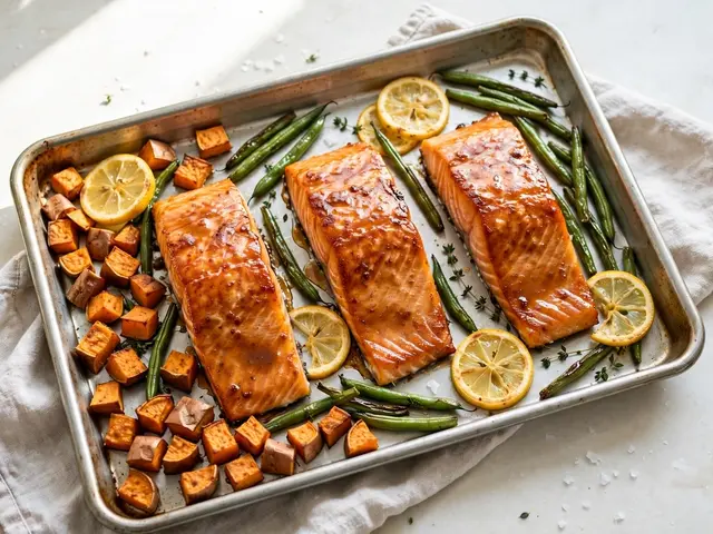 Metal baking sheet holds glazed salmon fillets, roasted sweet potatoes, green beans and lemon slices on a bright kitchen
