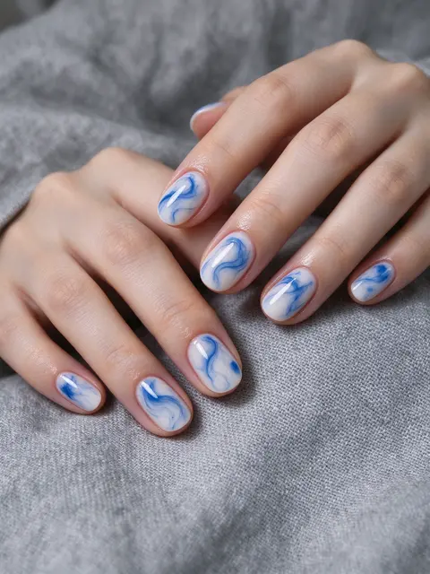 A woman's hands displaying blue and white marble gel manicure resting on gray linen fabric