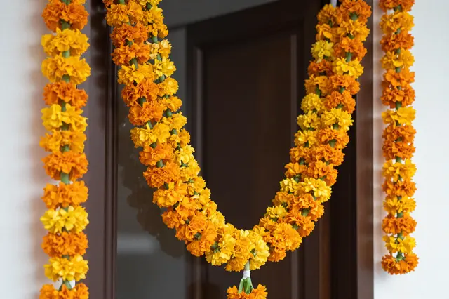 Bright orange and yellow marigold garlands hang decoratively around a dark wooden interior doorway.