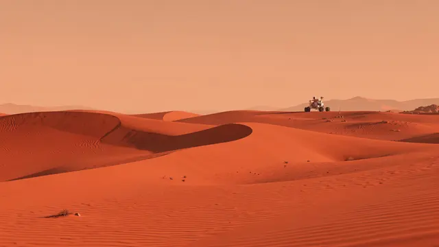 Red undulating Mars dunes stretch under a hazy orange sky with a robotic rover on a far ridge
