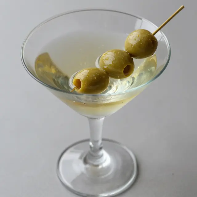 Chilled cloudy martini in a glass garnished with three green olives on a wooden pick