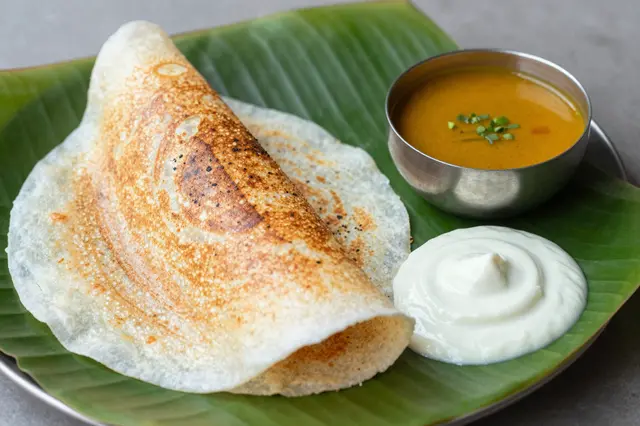 Crispy masala dosa served with sambar and coconut chutney on a fresh green banana leaf plate.