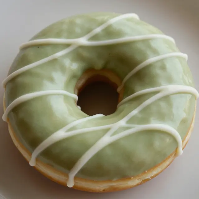 Top view of a single matcha glazed donut with white chocolate drizzle on a light neutral plate