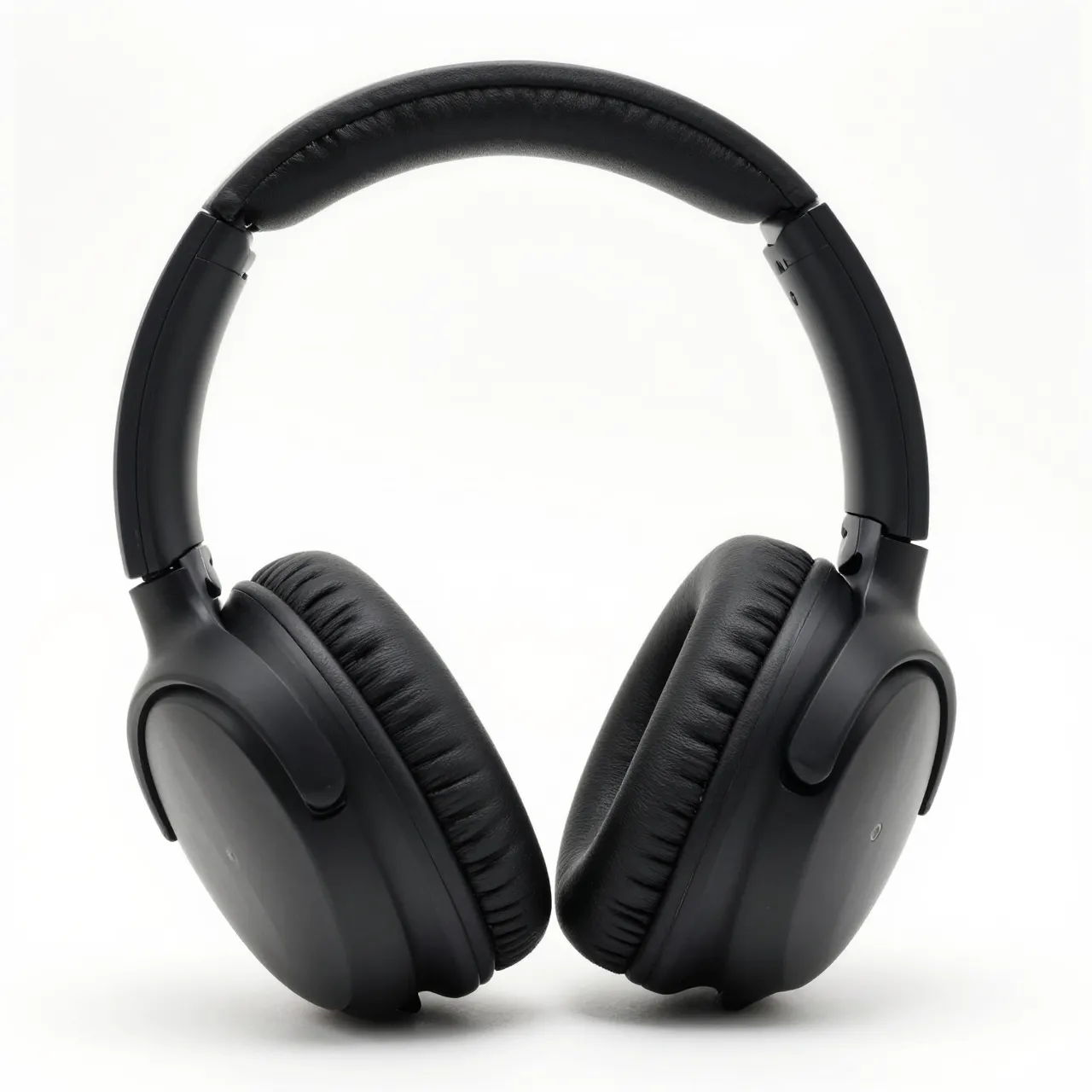 Plain matte black over-ear headphones rest against a pure white studio background.