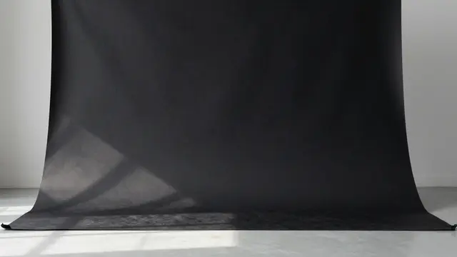A seamless matte black studio backdrop rests on a light gray floor with soft light pooling at its base.