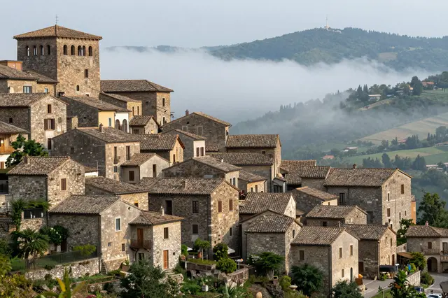 A stone medieval hill town overlooks a mist-shrouded valley in rural Italy