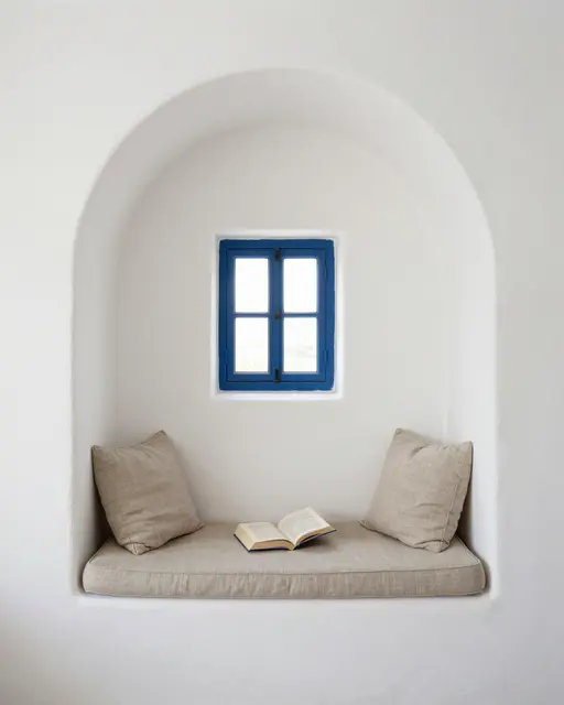 Built-in whitewashed arch reading nook with linen cushions, an open book, and a small blue window