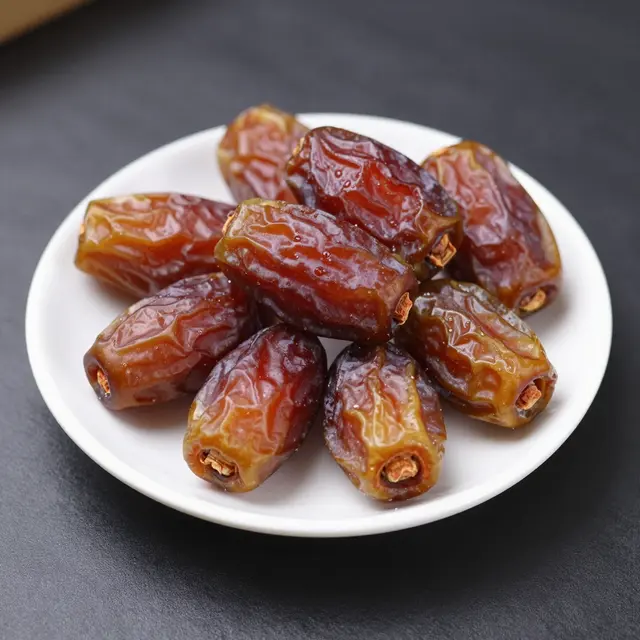 Whole glossy medjool dates arranged on a small white plate atop a dark matte surface