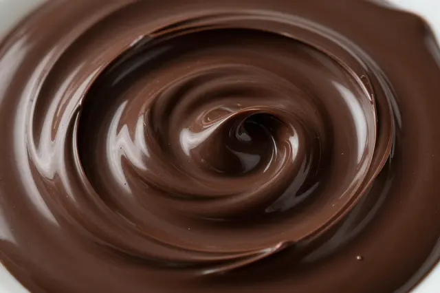 Close-up view of a glossy, spiraling swirl of smooth melted dark chocolate