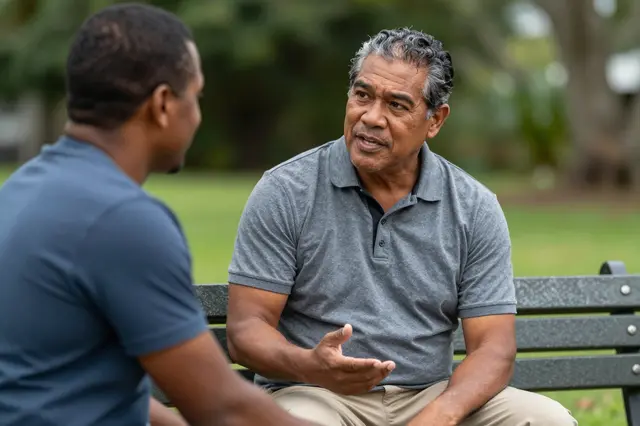 Two men sit on a park bench having an open casual conversation