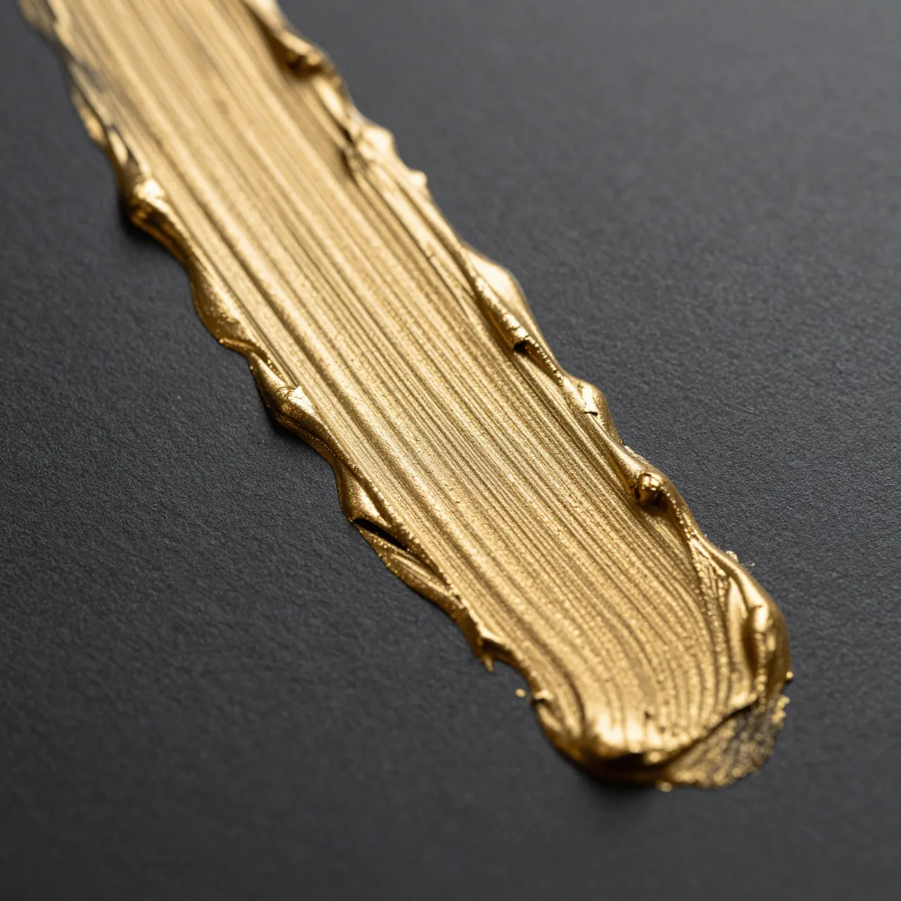 A close-up of a textured metallic gold paint drag across a matte dark charcoal surface.