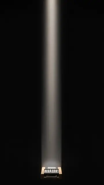 A small chip at the bottom of a dark frame projects a straight vertical beam of warm light upward against a black background
