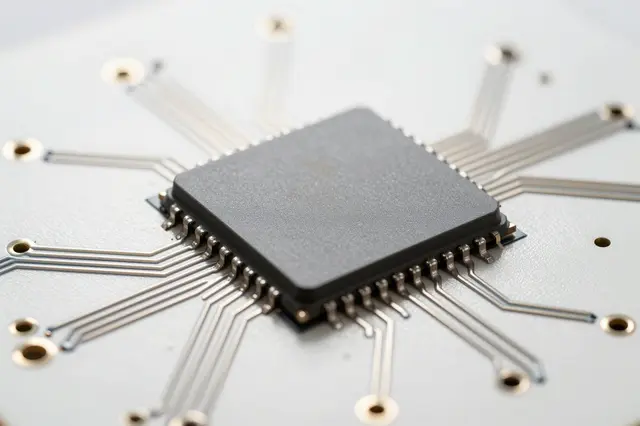 Close-up of a blank gray semiconductor chip mounted on a white circuit board with fanning silver traces.