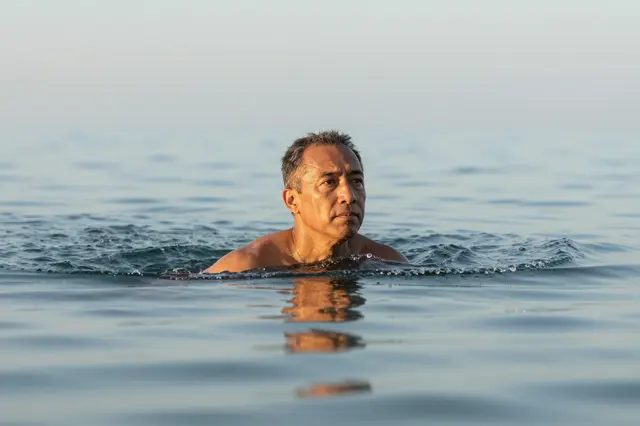 Mixed-race man in his fifties floats with his head above calm sea water at dawn
