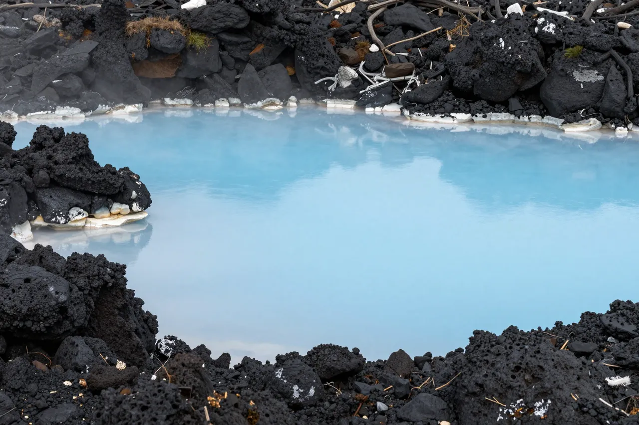 Steamy milky blue geothermal lagoon bordered by rough black volcanic lava rocks