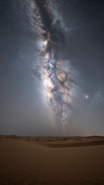 Bright milky way galaxy stretches across the night sky above rippled sand desert dunes