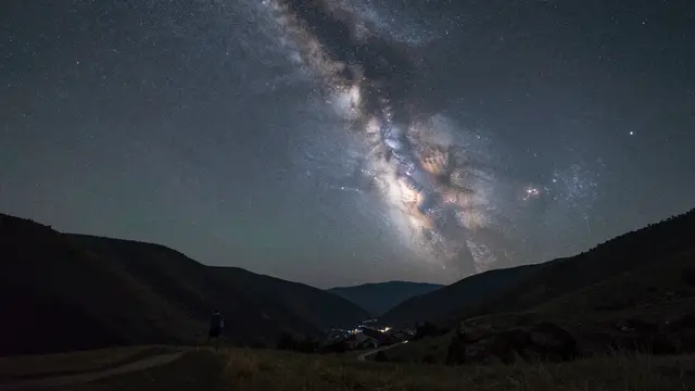 Bright milky way galaxy arches over a quiet mountain valley on a clear dark starry night