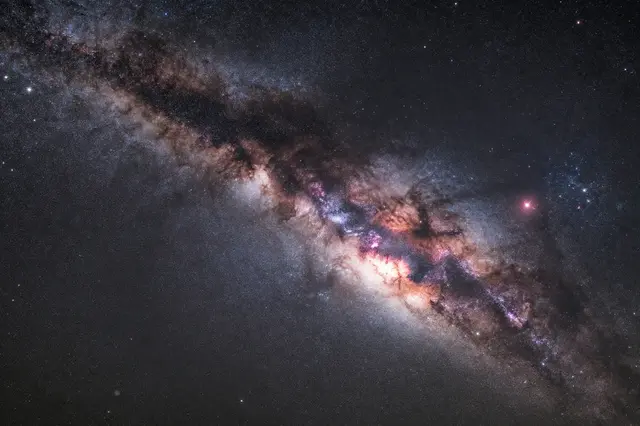 Dense star field of the Milky Way with glowing pink and warm nebula clouds against dark space