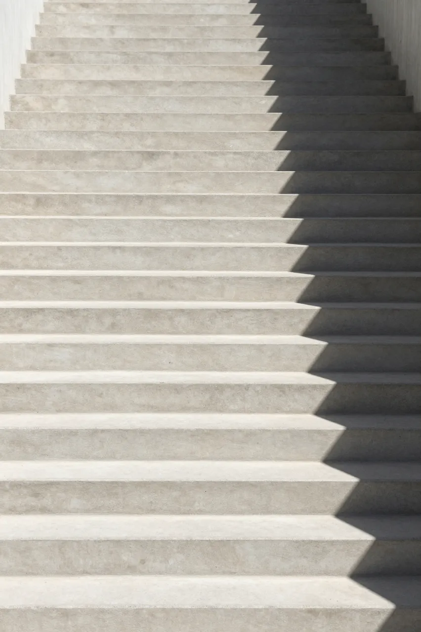 Pale concrete staircase with long sharp cast shadows extending upward through empty frame space