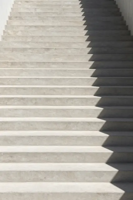 Pale concrete staircase with long sharp cast shadows extending upward through empty frame space