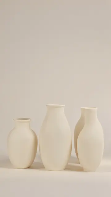 Four matte cream ceramic vases arranged in a row against a soft neutral beige background