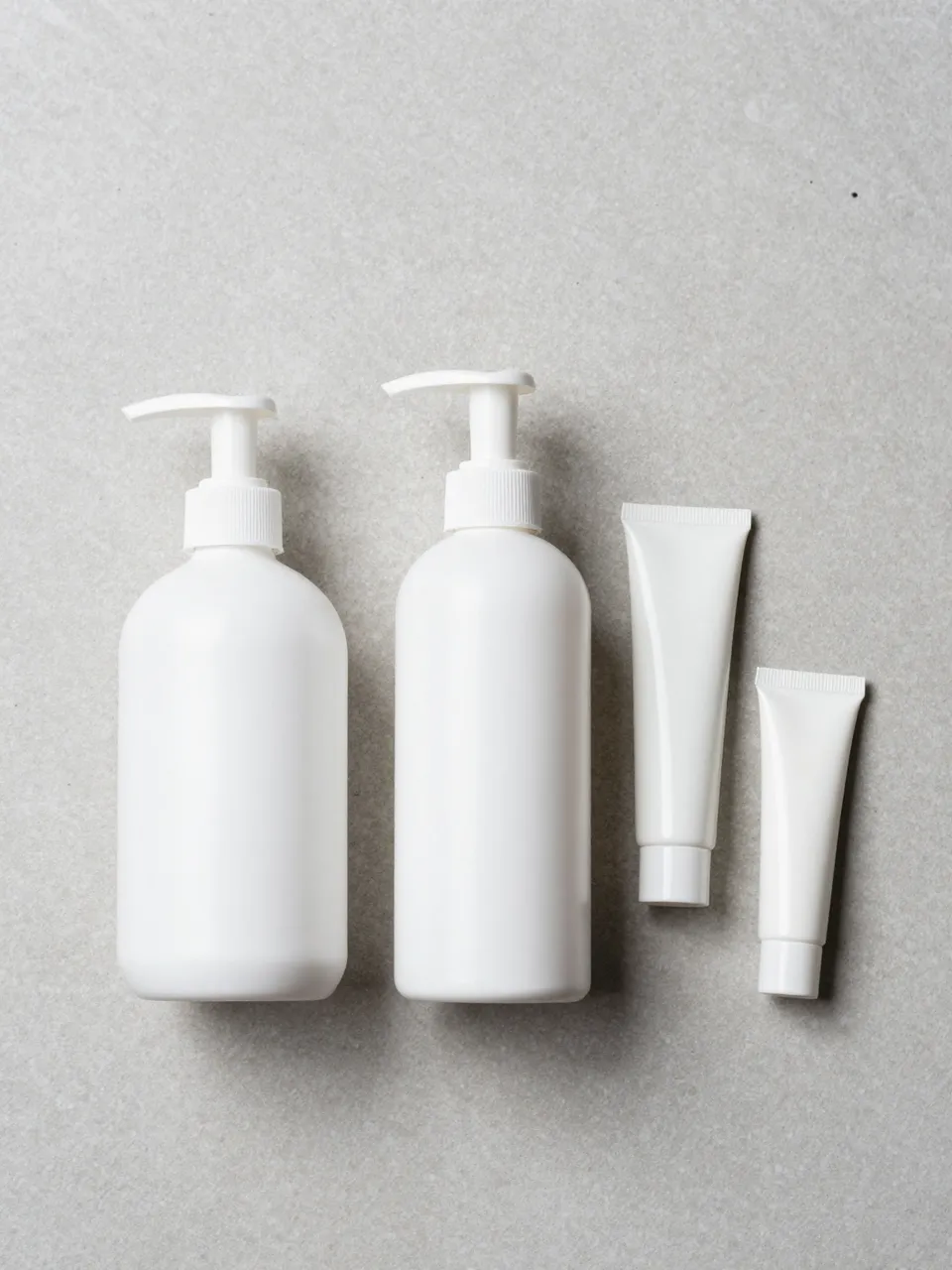 Plain white pump bottles and tubes arranged by size on a light gray stone surface
