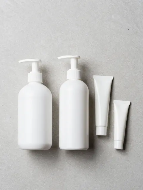 Plain white pump bottles and tubes arranged by size on a light gray stone surface