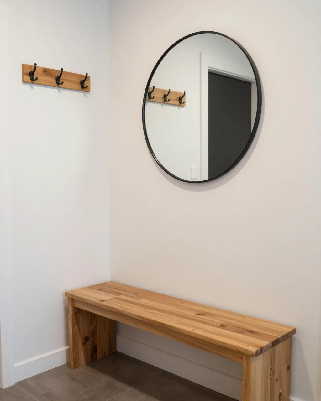 A tidy entryway corner features a wooden bench, wall hooks, and a round black-framed mirror above the bench.