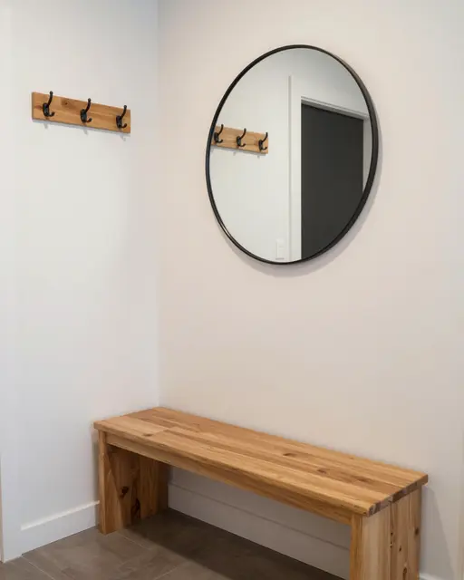A tidy entryway corner features a wooden bench, wall hooks, and a round black-framed mirror above the bench.