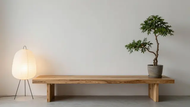 Low oak bench, lit paper floor lamp and potted bonsai sit against a plain light wall