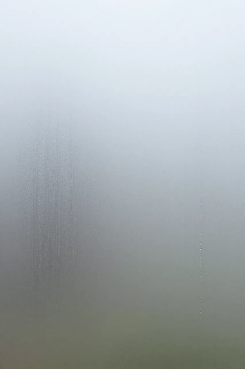 Close-up of fogged glass with faint vertical trickle streaks under soft diffused backlight