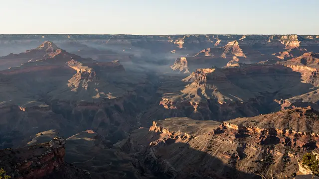 Layered canyon rock formations are illuminated by warm sunrise light with mist filling the deep valley