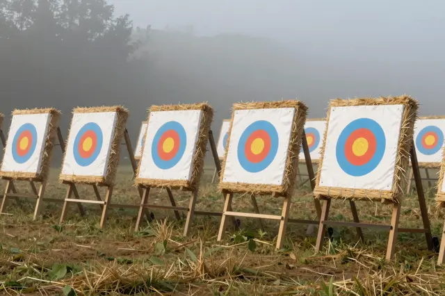 Row of straw archery targets stands in a foggy grass field at early morning